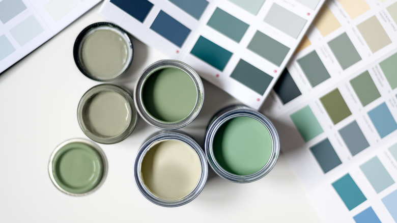 An aerial view of different shades of sage green paints open next to paint chips.