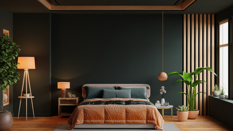 A bedroom with dark green walls and terracotta furniture and decor accents.