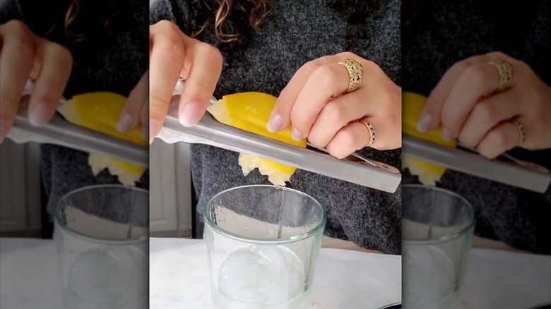woman juicing lemon into glass cup with old kitchen tongs