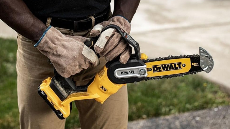 A man with gloves holding the yellow DeWalt chain saw.