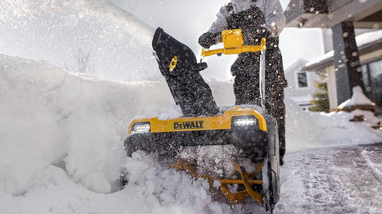 A man in overalls pushing the DeWalt snow blower through snow.