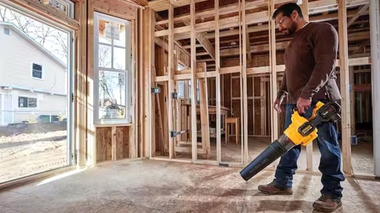 A man using the leaf blower inside a house being constructed.