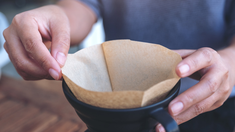 hands placing coffee filter over mug