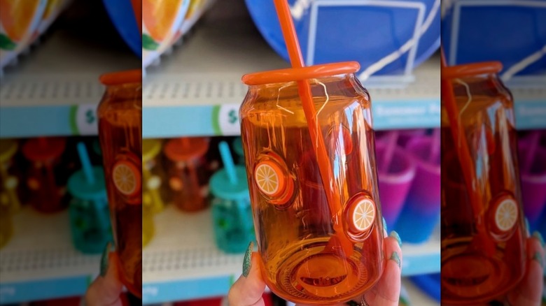 A person holds up an orange icon glass in front of Dollar Tree shelves