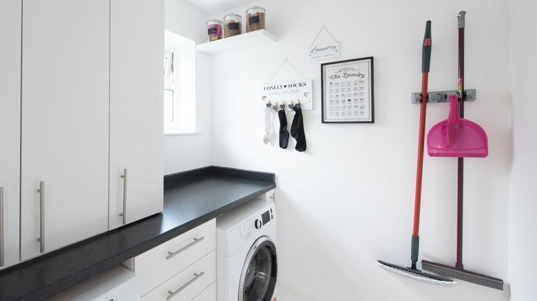 A white laundry room with a broom holder on the wall.