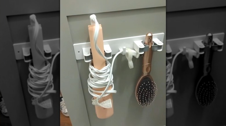 A Dollar Tree Broom Holder being used to hold hair tools on the back of a cabinet door.
