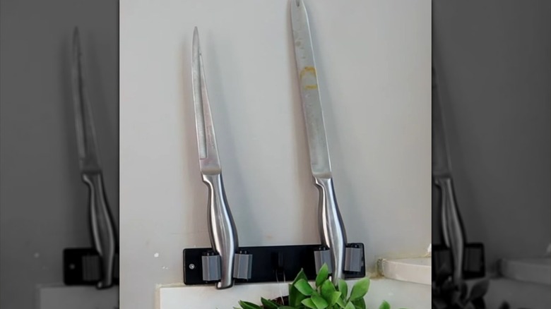 Two silver knives rest in a Dollar Tree Broom Hanger on the wall.