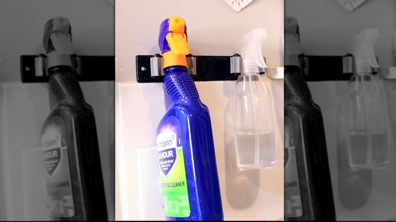 A Dollar Tree broom holder holds two cleaning spray bottles.