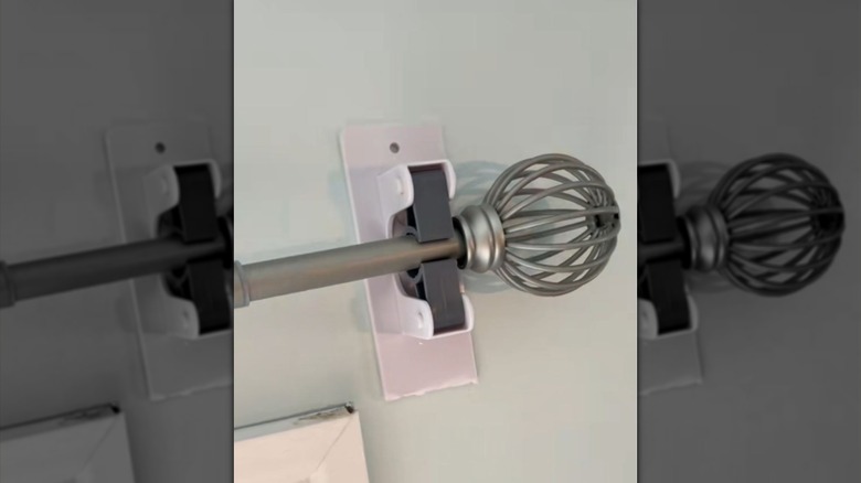 Half of a Dollar Tree broom holder holds a curtain rod above a window.