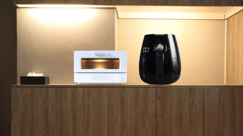 A modern design toaster oven and black air fryer on a wooden table
