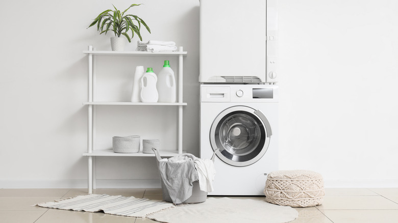 Interior of laundry room with modern washing machine and clothes dryer near white wall