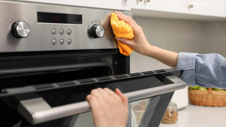 Woman cleaning electric oven with rag in kitchen