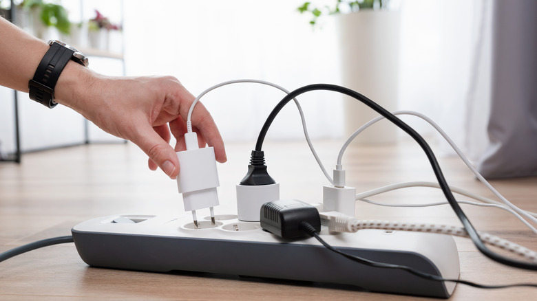 Someone plugging in a cord to a power strip with other things plugged into it.