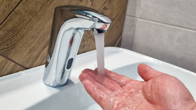 a man's hand under a stream of water from the tap in the sink