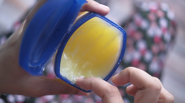 Top down view of hands touching petroleum jelly in a container with a blue lid