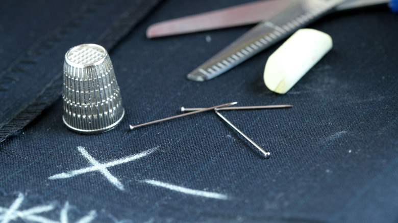 Tailor's chalk on top of fabric with a thimble, pins, and scissors
