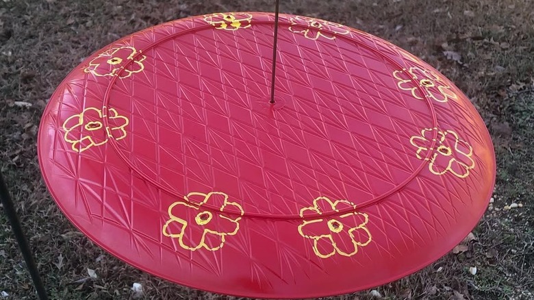 Hummingbird feeder made from red charger tray and wire with painted yellow flowers on top