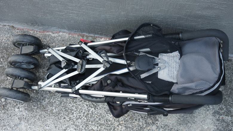 Folded up baby stroller, laying on concrete against a house wall