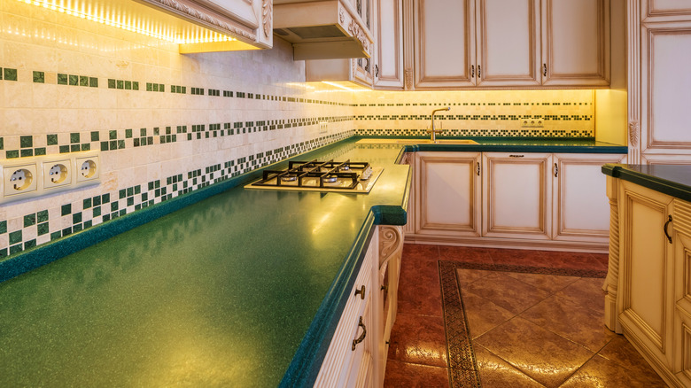 A kitchen with dark green countertops and ornate white and gold cabinets