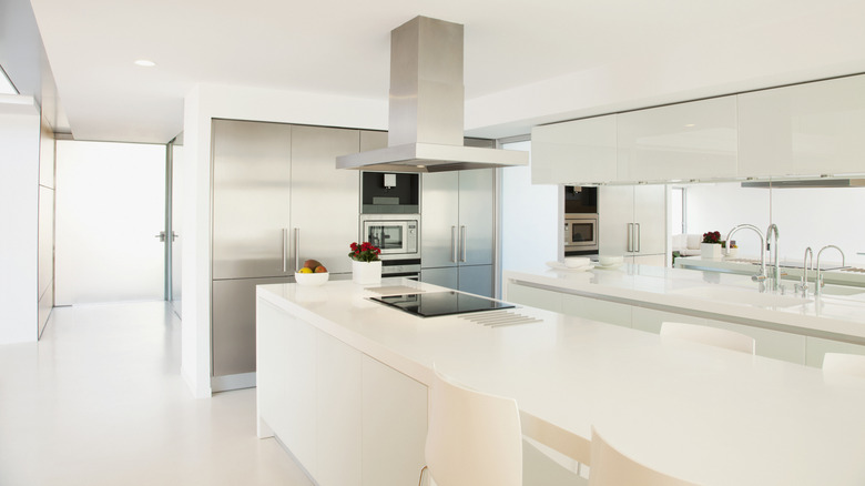 A very white kitchen with stainless steel appliances, white countertops, and white flooring