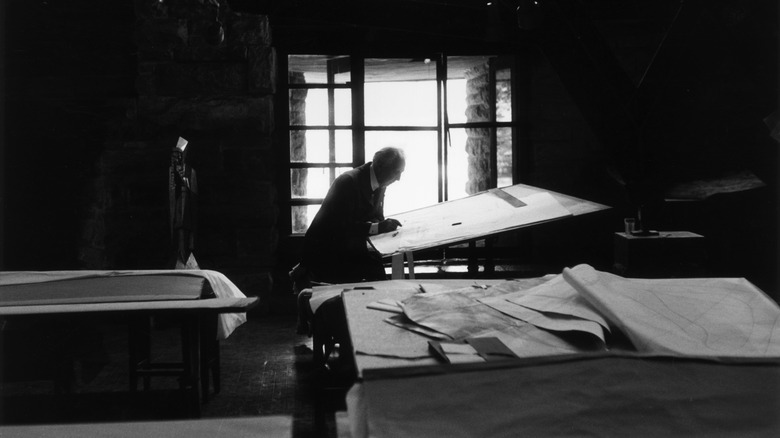 A black and white photo of Frank Lloyd Wright sitting at his drafting table in Arizona.