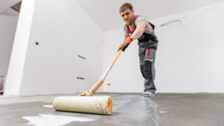 professional worker using roller to prime concrete floor