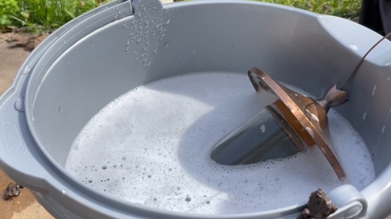 A hummingbird feeder inside a bucket filled with soapy solution