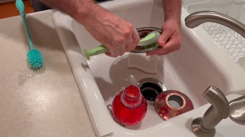 Ungloved hands cleaning the base of hummingbird feeder with a large brush