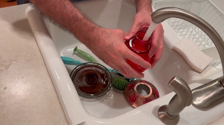 Hands rinsing out a hummingbird feeder in a sink