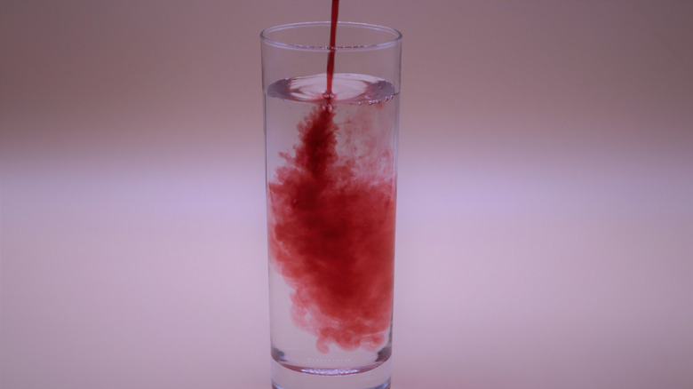 Red liquid mixing into a glass of water