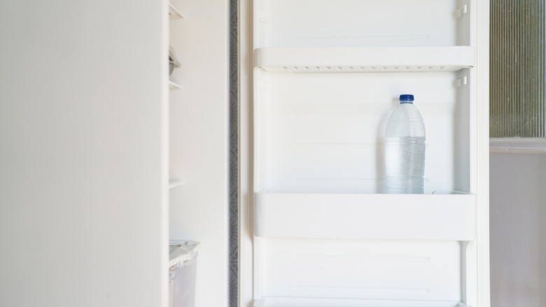 An opened white fridge with unlabeled bottle of water in the door