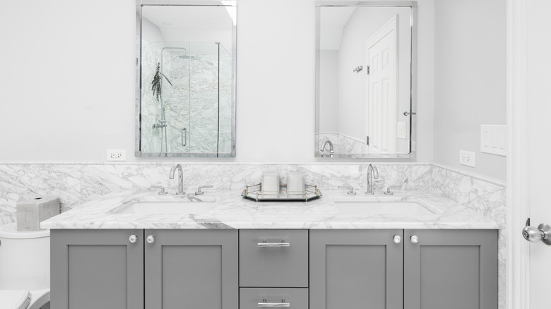 A bathroom with marble counter tops and grey cabinets