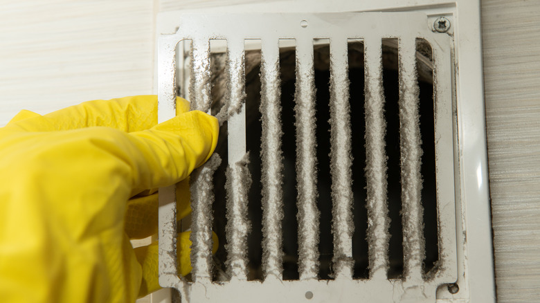 Gloved hand removing dusty air vent cover