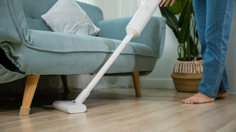 Person vacuuming wood floor under sofa