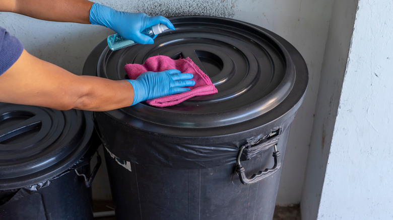 Person cleaning garbage can lid with spray and cloth