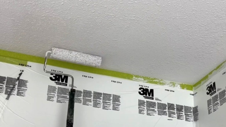 person painting popcorn ceiling white with paint roller