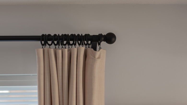 black curtain rod for window curtains, with beige or brown curtain against the background of a window and a white wall, interior in the style of cozy minimalism