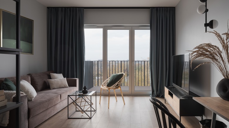 Simple and stylish living room with cozy couch, modern furniture, tv and window doors to balcony