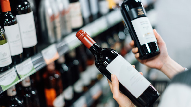Woman choosing between two bottles of wine in supermarket