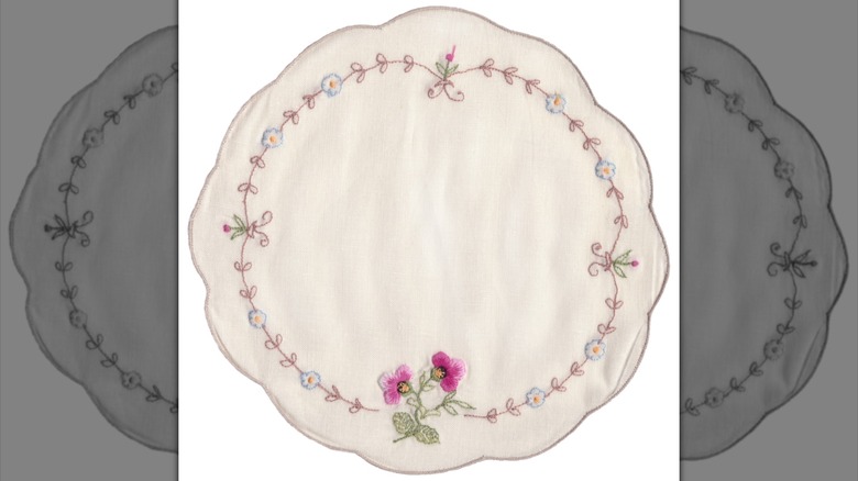 A scalloped, round, embroidered doily on a white background.