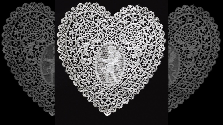 A heart-shaped, lace doily on a black background.