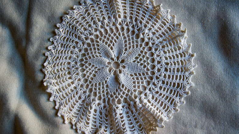 A round spider-web inspired crochet lace doily sitting on a cloth.