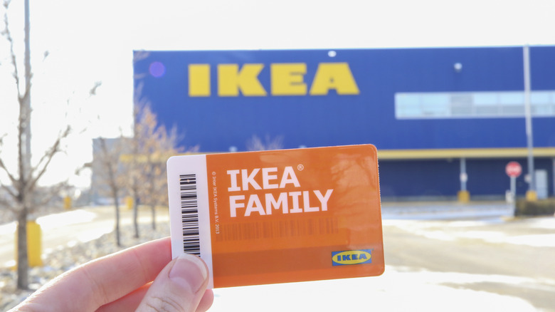 Hand holding an IKEA Family card in front of an IKEA storefront