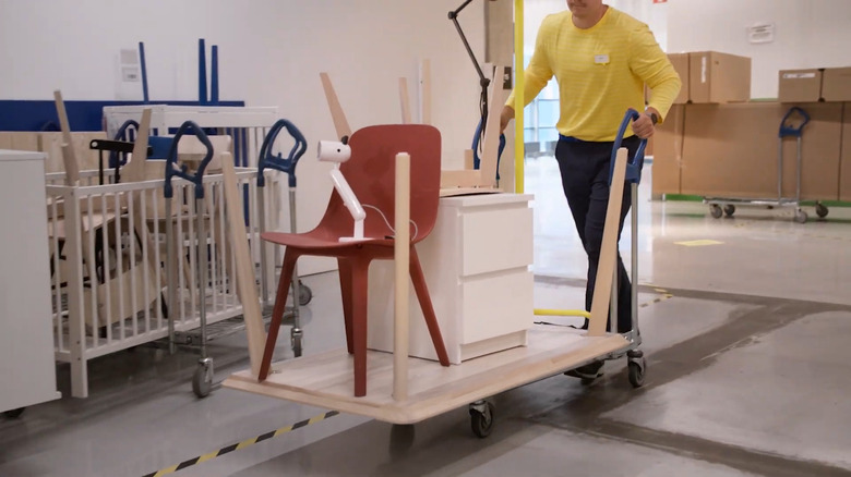 IKEA worker pushes chair, lamp, and small nightstand on a cart in a store