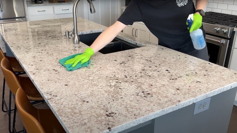 man wiping granite counter with green gloves and microfiber cloth