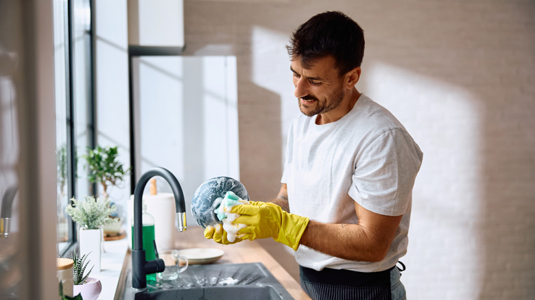 handsome man scrubbing dishes in clean home with yellow gloves