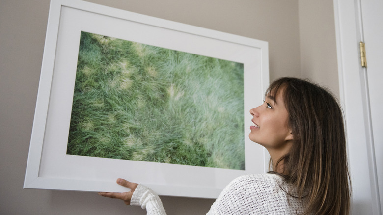 A woman hangs a framed print on the wall.
