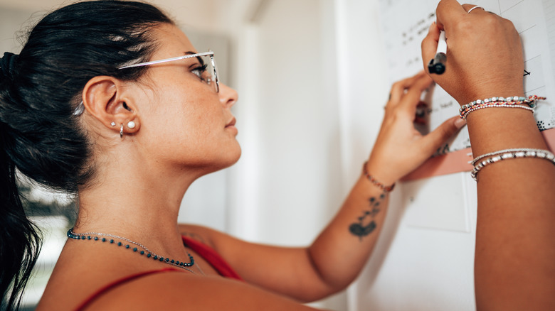 A woman writes on paper wall calendar.