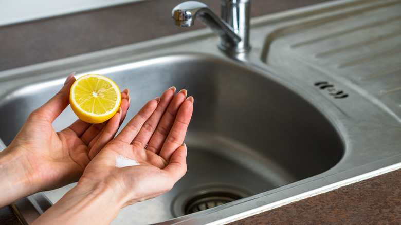 woman holding lemon and salt over a stainless steel sink preparing to clean
