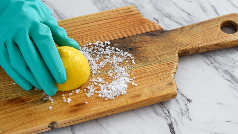 person cleaning a cutting board with coarse salt and lemon